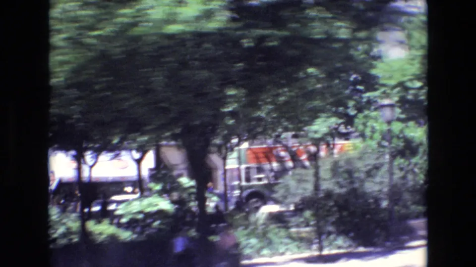 1972 Portugal home-movie frame showing a motion-blurred urban roadside with leafy trees, cars, and building frontage seen from a passing vehicle.