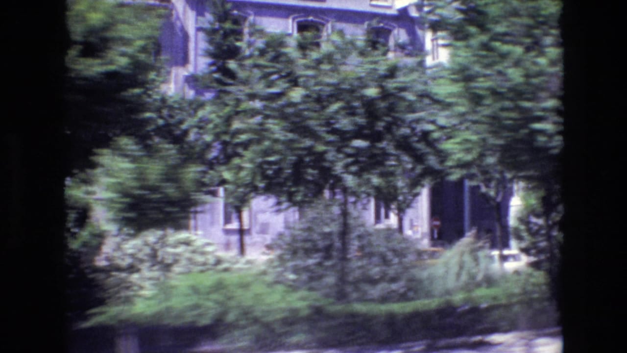 1972 Portugal street view with a residential facade, shrubs, trees, and a dark entrance glimpsed from a moving car.