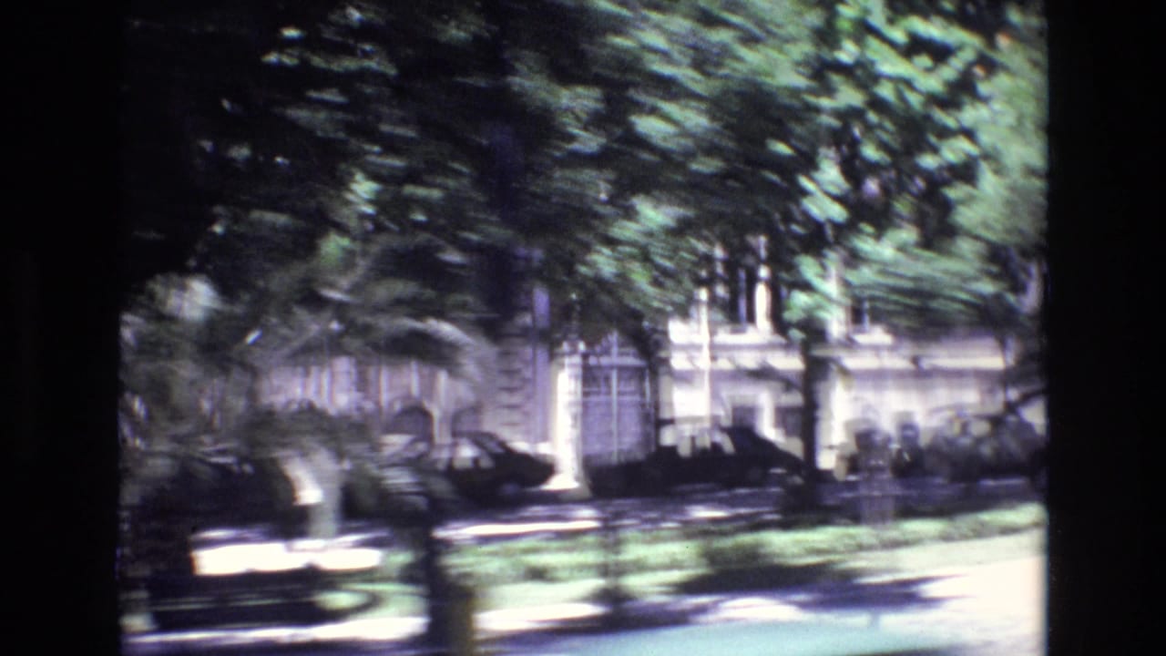 1972 Portugal home-movie frame showing a sunlit urban street through trees, with parked cars, building facades, and motion blur from a moving vehicle.