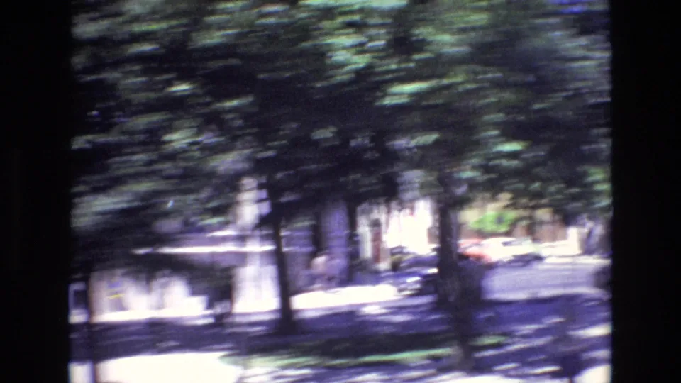A moving 8mm view in Portugal in 1972 appears to pass trees and parked cars along a bright urban street, with heavy motion blur across the frame.
