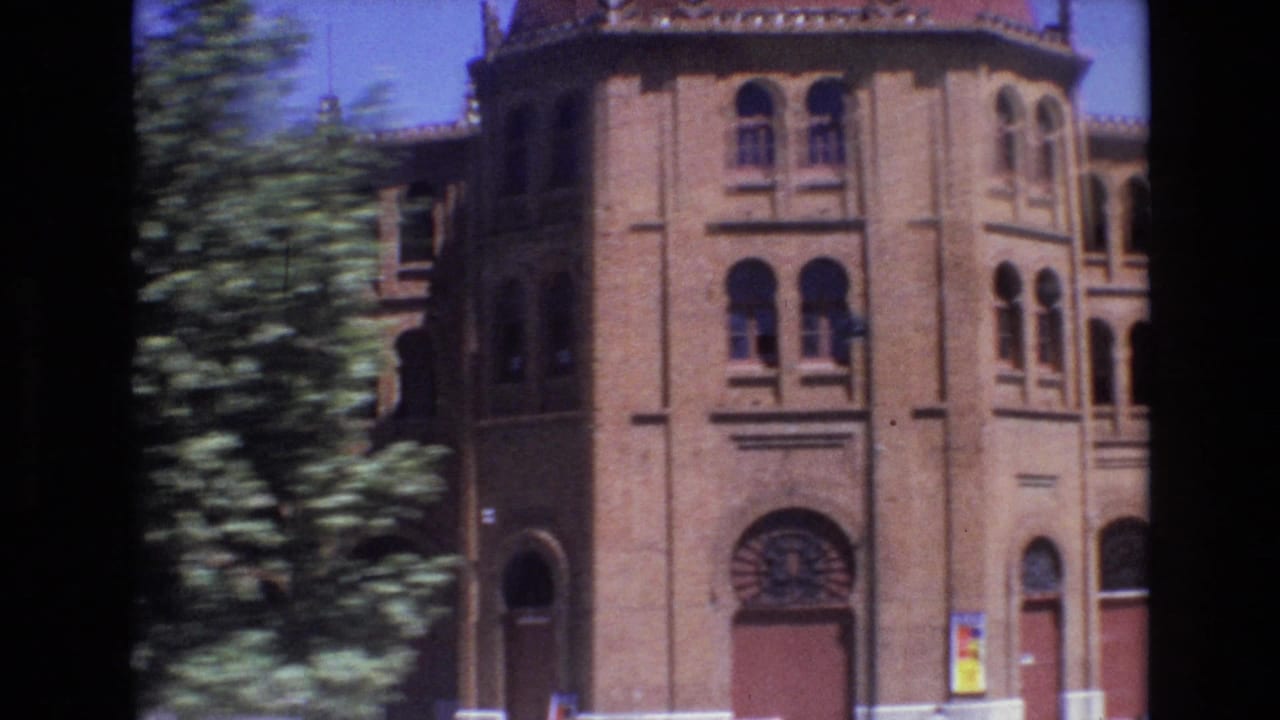 A brick urban building in Portugal, filmed in 1972, with arched windows, red doors, surrounding trees, and bright sunlit exposure.