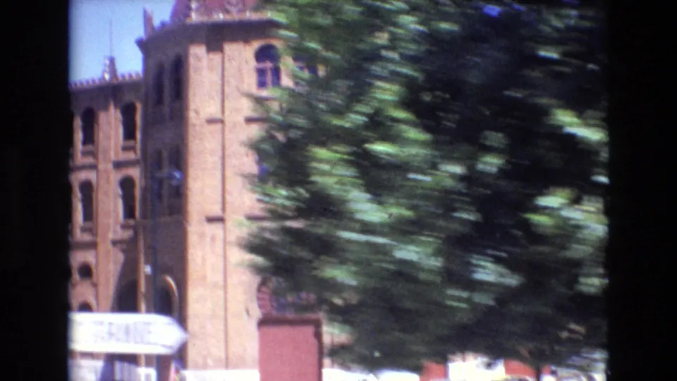 A moving 8mm view of a brick building in Portugal, partly hidden by passing trees and showing strong blur from the camera movement.