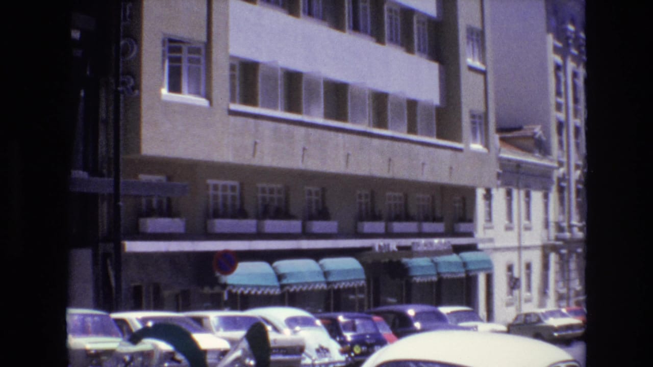 A row of parked cars sits beneath teal awnings on a city street.