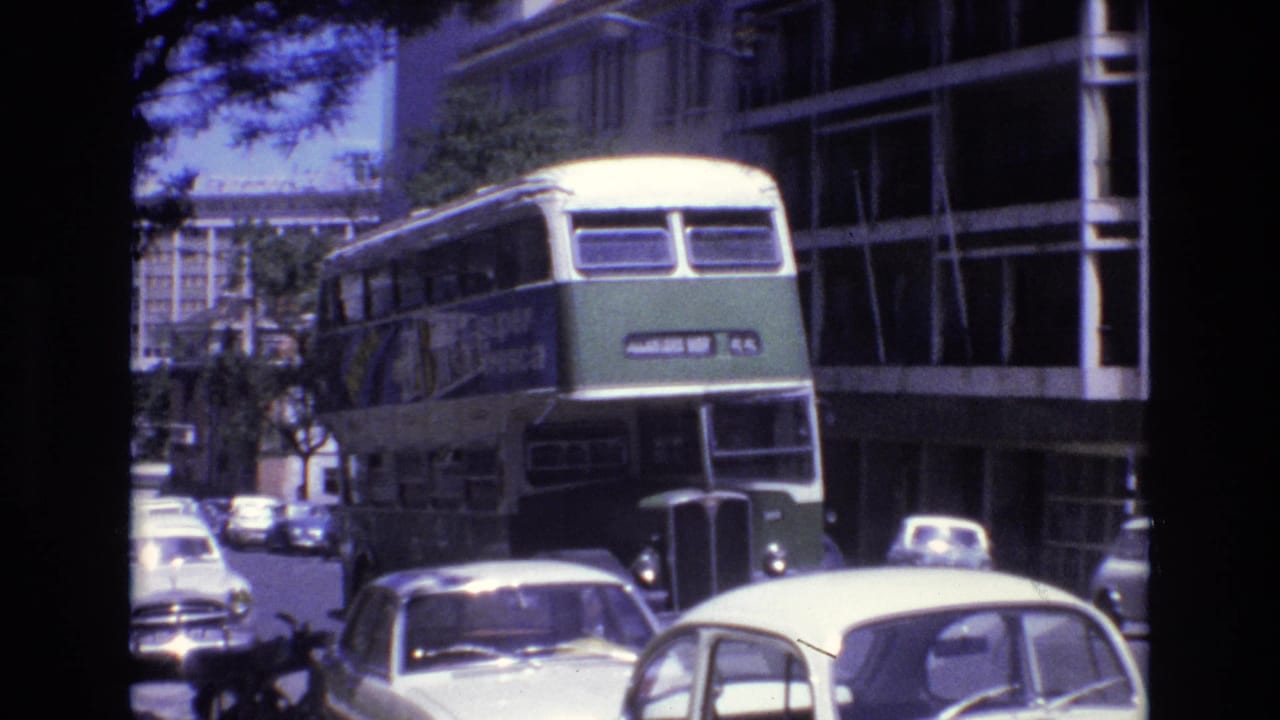 Green and cream double-decker bus approaching through city traffic.