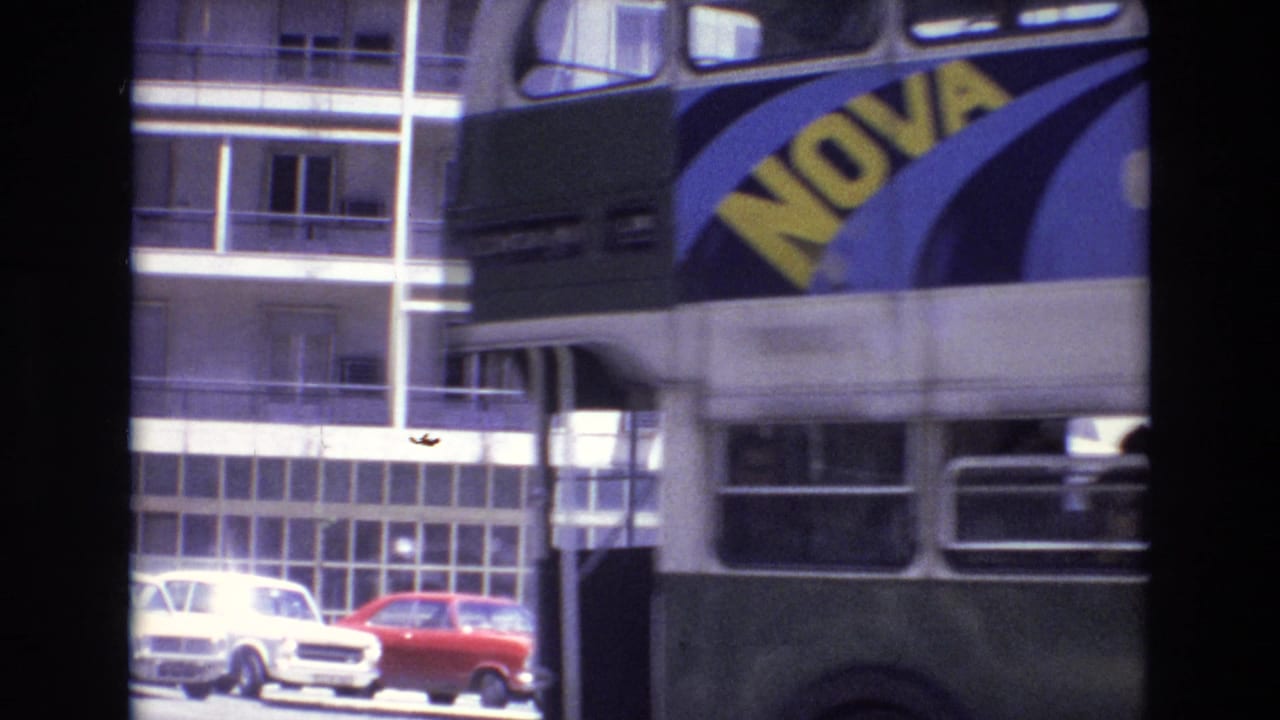 1972 Portugal street view with a green and cream double-decker bus carrying a NOVA advertisement beside apartment buildings and parked compact cars.