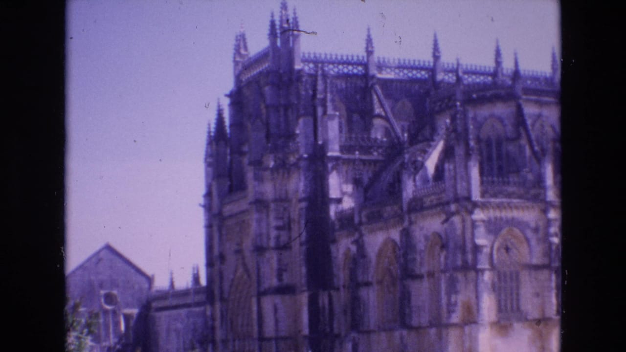 1972 Portugal 8mm frame showing a historic stone church facade with Gothic-style arches, roof pinnacles, and soft purple-blue film color.