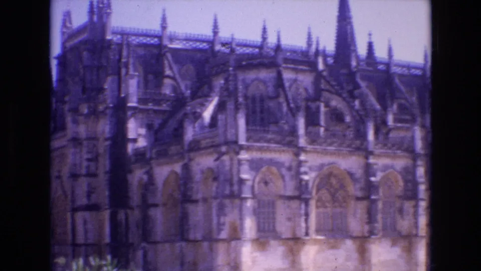 1972 Portugal 8mm frame showing the church facade closer in view, with pointed window forms, stone tracery, pinnacles, and purple color fading.