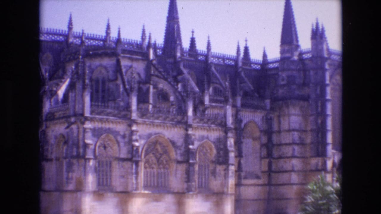 1972 Portugal 8mm frame showing a Gothic cathedral exterior with pointed stone arches, spires, tracery, and a pale sky above the facade.