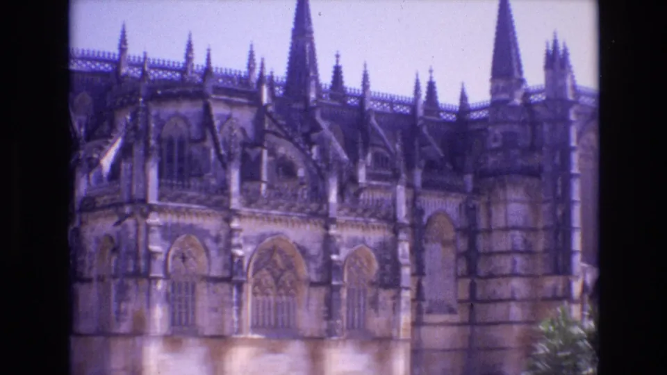 1972 Portugal 8mm frame showing a Gothic cathedral exterior with pointed stone arches, spires, tracery, and a pale sky above the facade.