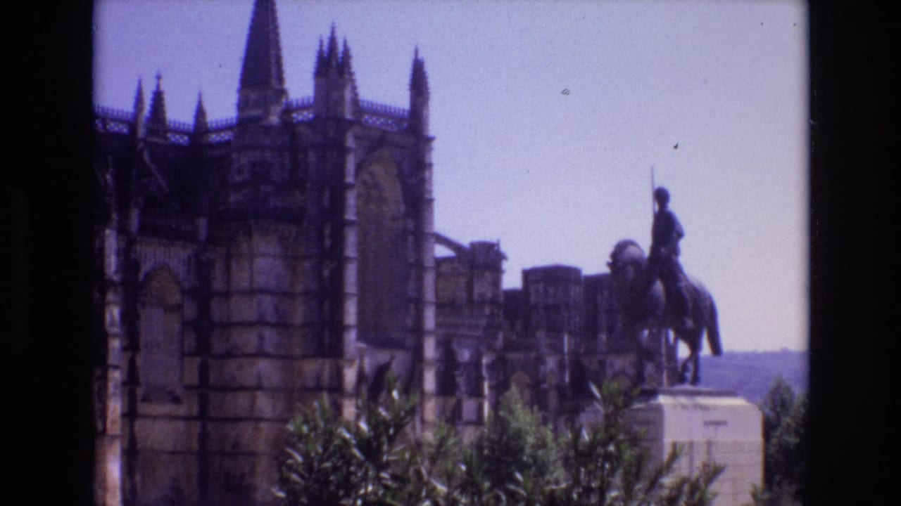 1972 Portugal 8mm frame showing a rider-on-horseback statue in front of a Gothic-style stone building, with foliage in the foreground and pale sky behind.