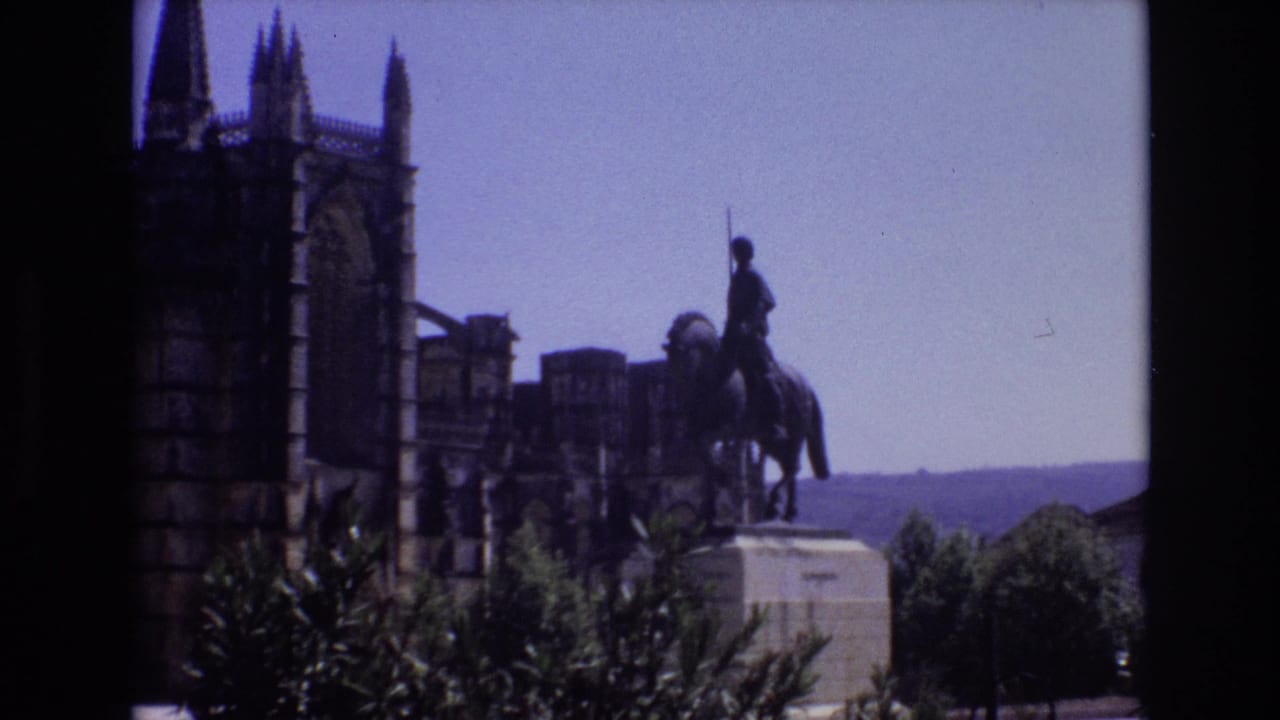 1972 Portugal 8mm frame showing an equestrian statue on a stone pedestal before a Gothic cathedral facade, with trees and distant hills behind the plaza.