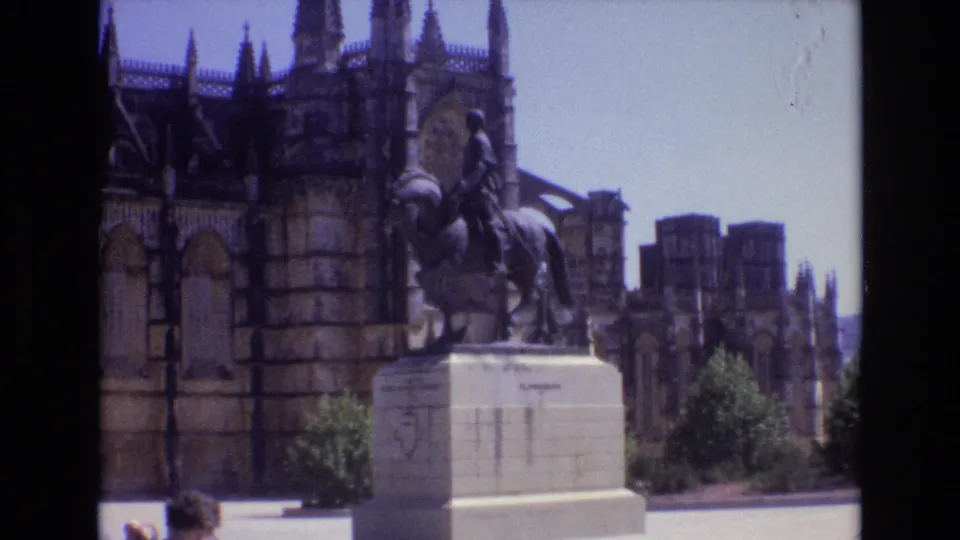 1972 Portugal 8mm frame with the horseback monument centered against a Gothic cathedral exterior, with a small partial visitor visible near the lower edge.