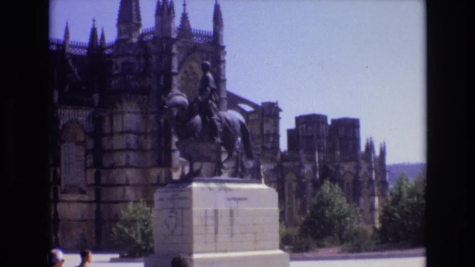 1972 Portugal travel-film frame showing an equestrian statue before a grand stone cathedral facade with towers and arched details.