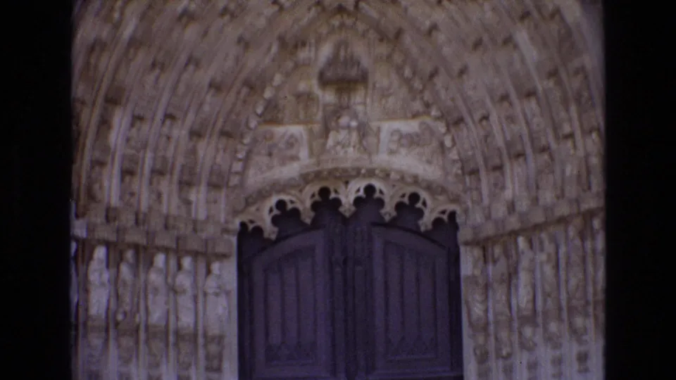 The camera tilts toward the cathedral's carved arched doorway, emphasizing the stone reliefs and closed upper panels of the wooden doors.