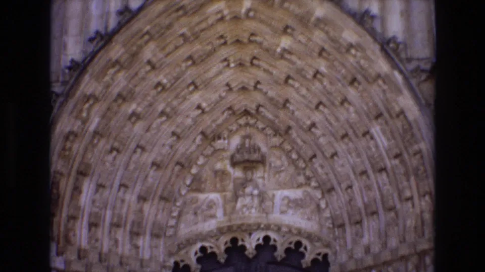 1972 Portugal 8mm frame focused on the upper carved stonework of a historic church entrance, with sculpted figures and layered arch details.