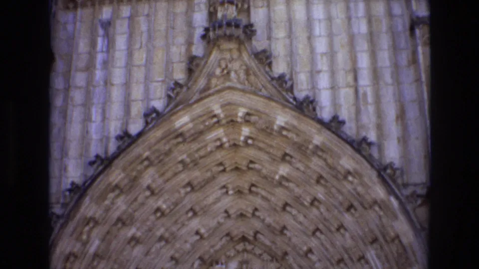 1972 Portugal 8mm frame looking up at the carved pointed arch and surrounding stone facade of a historic church entrance.