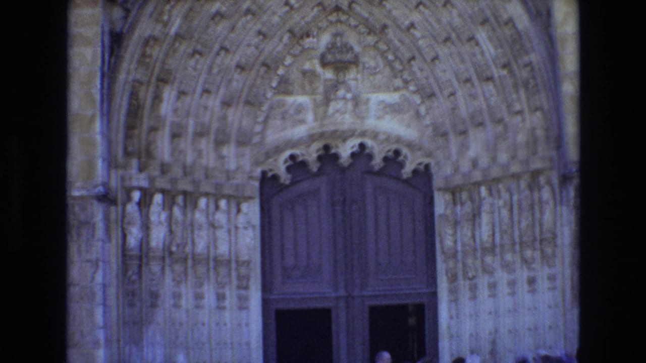 1972 Portugal 8mm frame showing an ornate Gothic church portal with carved stone arches, statues, large dark wooden doors, and partially visible visitors near the entrance.