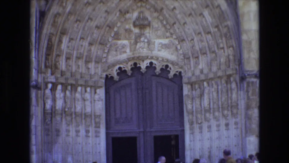 1972 Portugal 8mm frame holding on the cathedral's carved Gothic entrance, with the large wooden doors centered and visitors partly cropped at the lower edge.