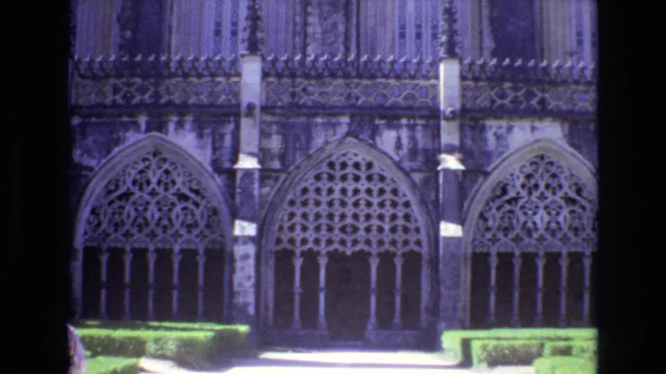 1972 Portugal 8mm frame centered on Gothic-style arched windows and carved stonework above clipped hedges, with a partial visitor figure at the lower left edge.