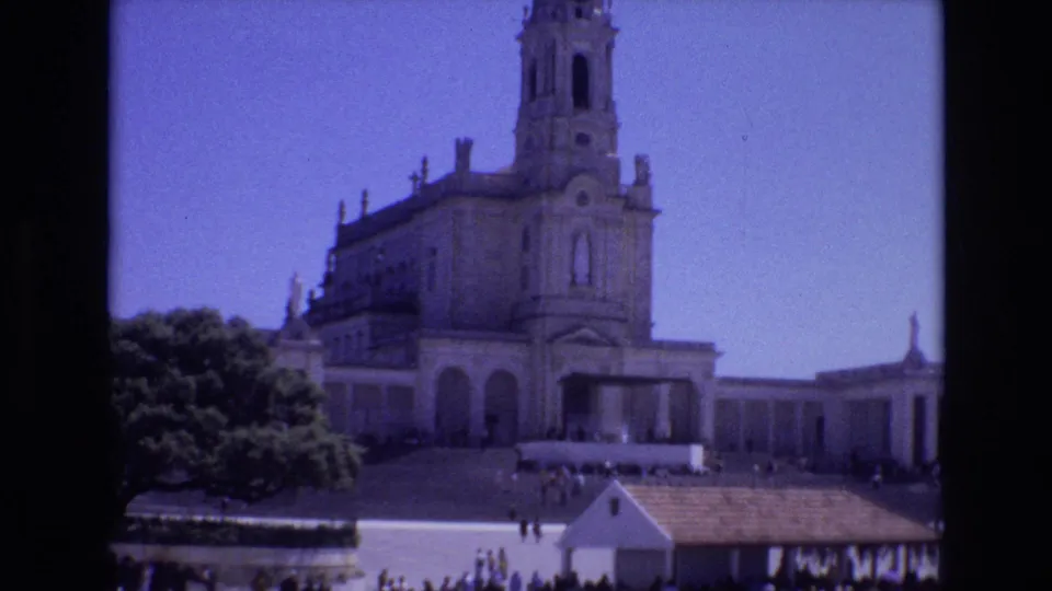 1972 Portugal 8mm wide shot of a large Catholic church or basilica facade with a central tower, open forecourt, trees, and small visitors on the grounds.