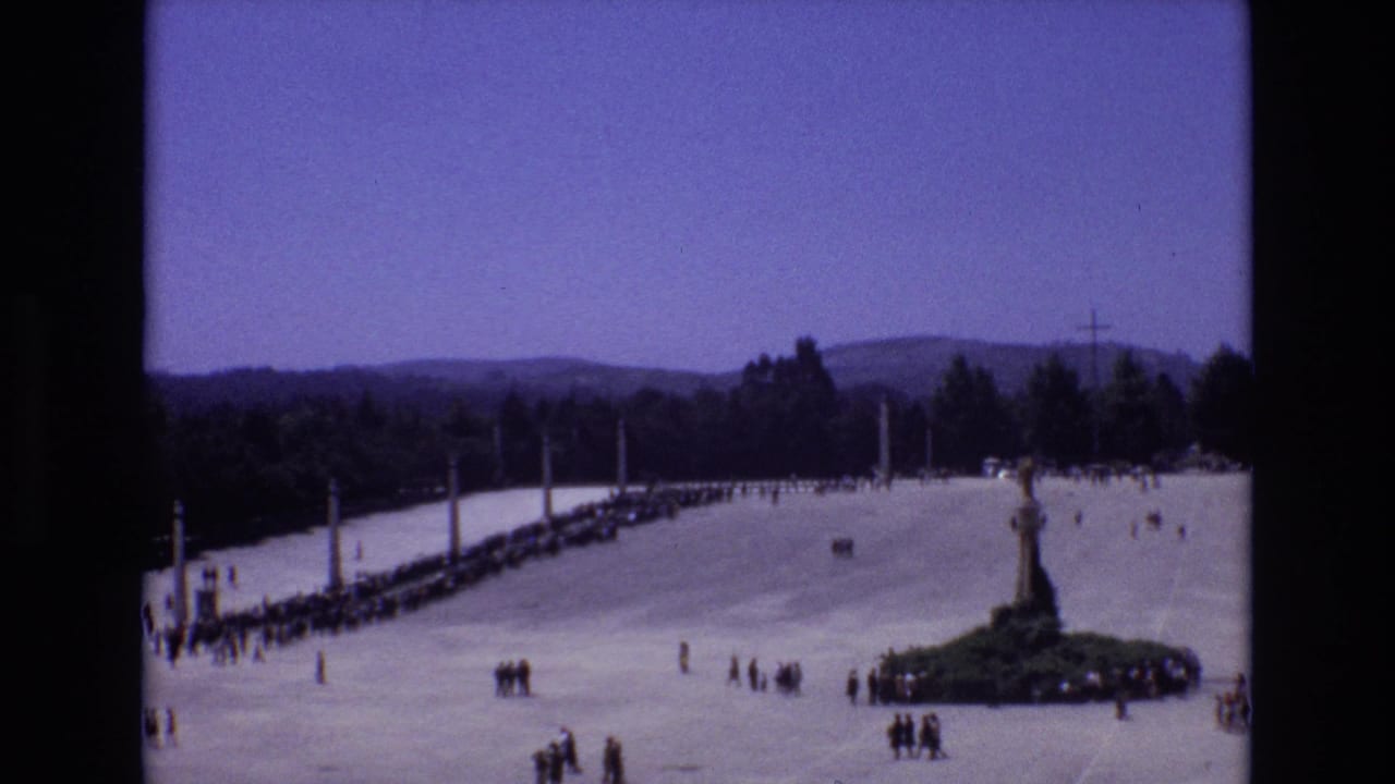 Wide plaza with a central monument, visitor lines, and distant hills.