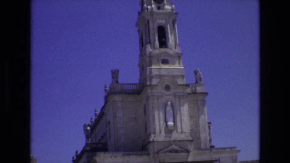 1972 Portugal 8mm frame emphasizing the cathedral bell tower and upper facade, with decorative stone details silhouetted against a saturated blue sky.