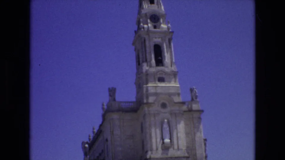 1972 Portugal travel-film frame showing the cathedral bell tower, upper stone facade, sculptural details, and clear sky in a slightly soft handheld composition.
