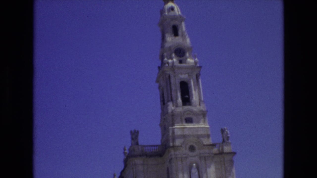1972 Portugal 8mm frame showing the upper portion of an ornate stone church tower with arched openings and sculptural roofline details against a blue sky.