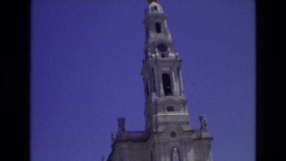 1972 Portugal 8mm frame showing the upper portion of an ornate stone church tower with arched openings and sculptural roofline details against a blue sky.
