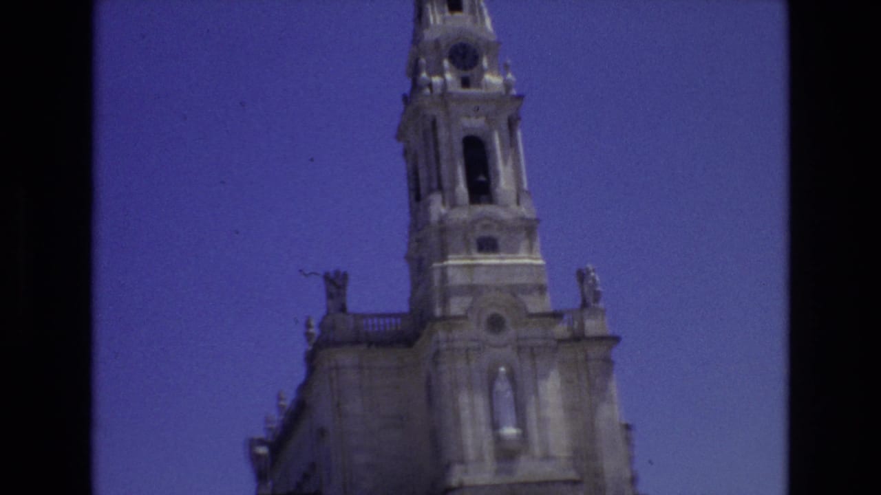 1972 Portugal 8mm frame with a low-angle view of a church tower, arched openings, roofline statues, and pale stonework under a saturated blue sky.