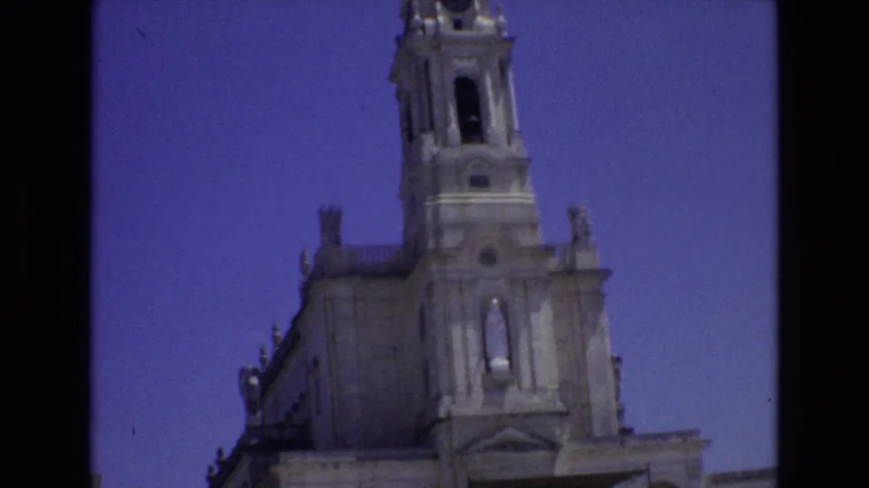 1972 Portugal 8mm frame showing a handheld low-angle view of a church tower and expanded facade with decorative stonework and religious statuary.