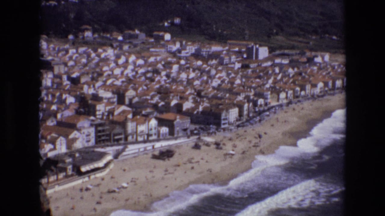 Aerial view of a coastal town beside a sandy beach with waves breaking offshore.