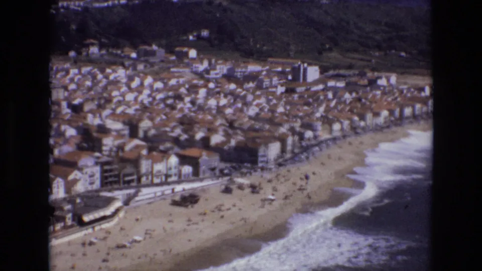 1972 Portugal 8mm closing frame of a seaside town and beach, with waves breaking along the shore and small figures visible on the sand.