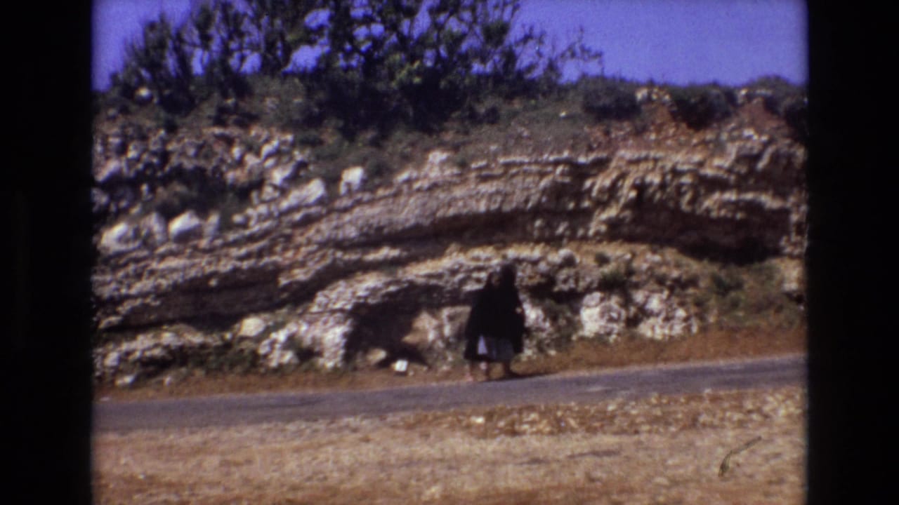 Two distant women walking near a rocky roadside embankment.