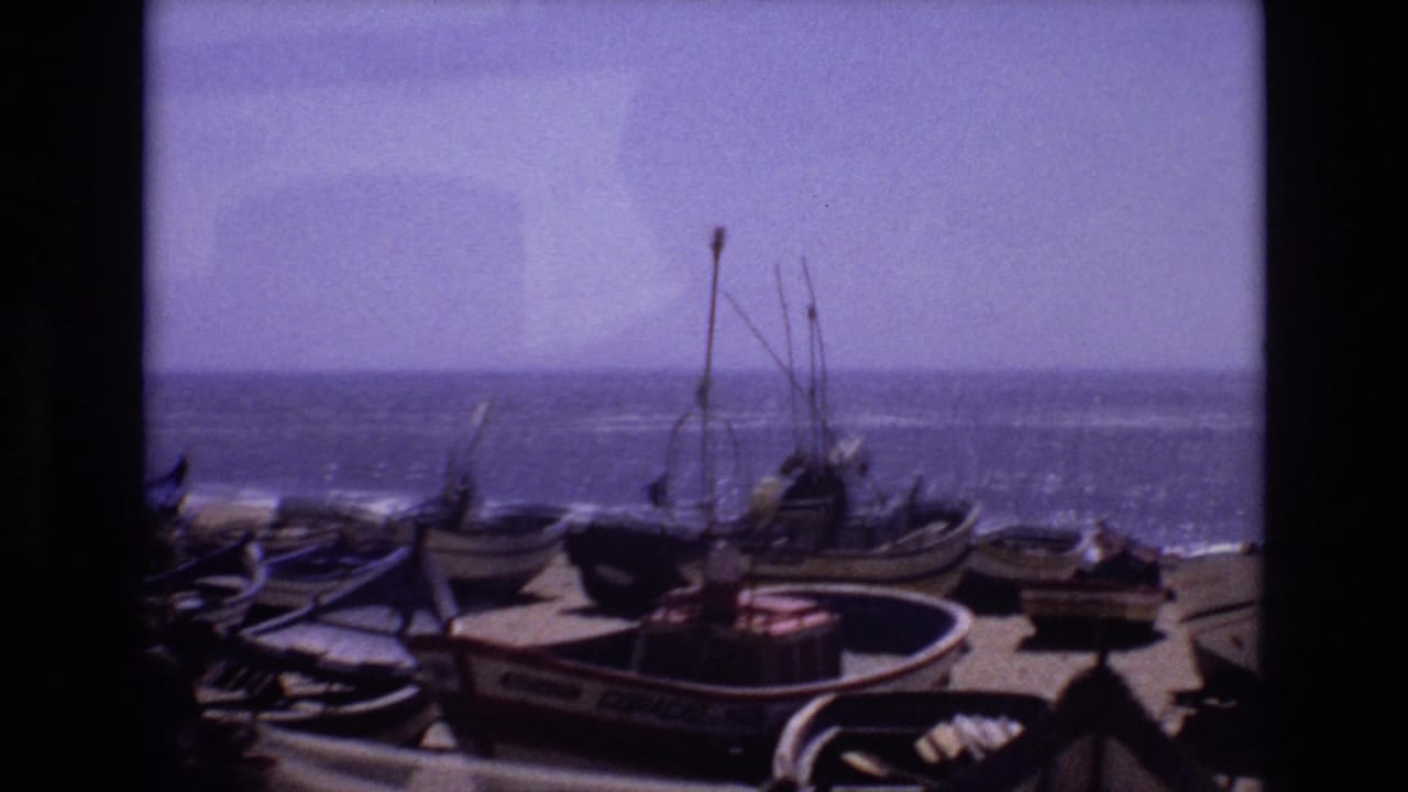 1972 Portugal coastal frame with several small boats on sand, upright rigging, painted hull lettering, and a bright ocean horizon under a pale sky.