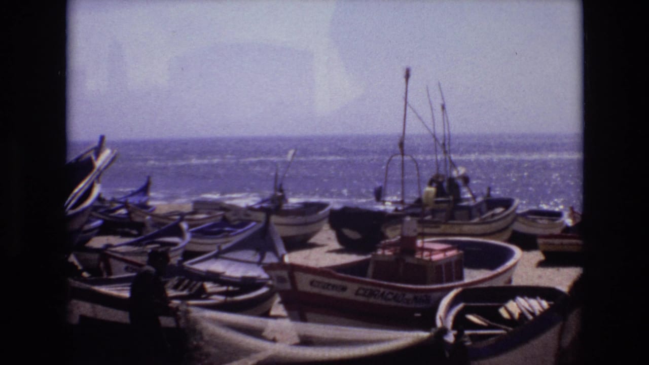 1972 Portugal 8mm frame showing small fishing boats on a sandy coastal shore, with gear in the foreground and the ocean beyond.