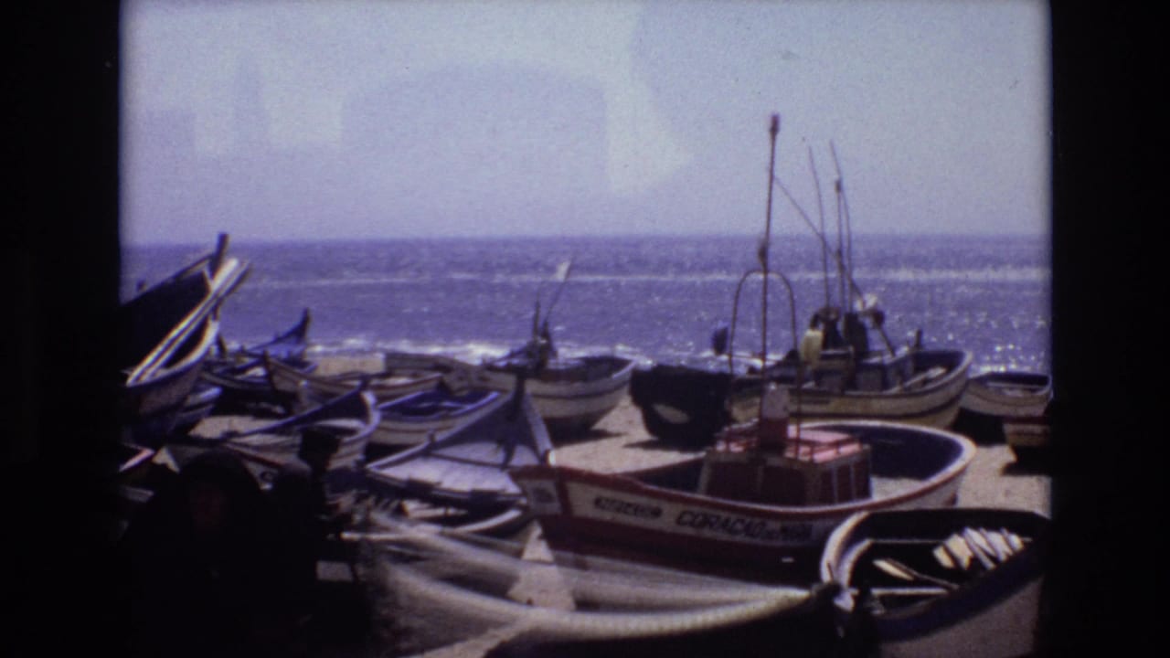 1972 Portugal home-movie frame of clustered small boats, visible rigging, and shoreline gear against a bright ocean horizon.