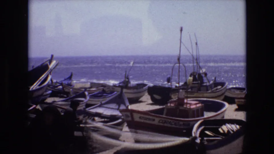 1972 Portugal home-movie frame of clustered small boats, visible rigging, and shoreline gear against a bright ocean horizon.
