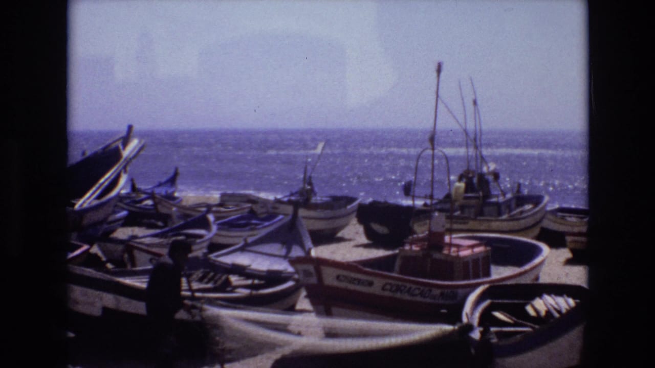 1972 Portugal home-movie frame showing wooden fishing boats pulled onto a sandy beach, with workers near the boats and the ocean behind them.