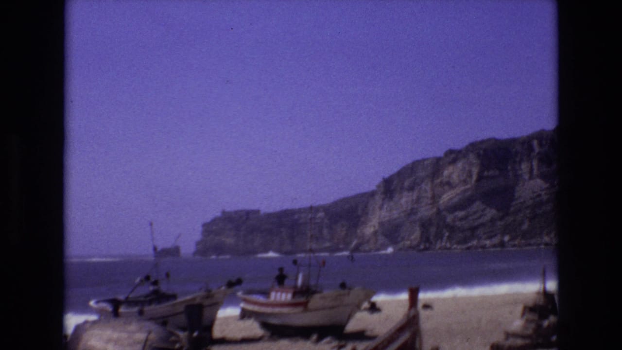 Small boats on a sandy Portuguese beach with cliffs and surf in the background.