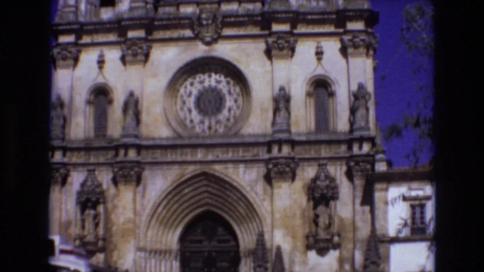 1972 Portugal 8mm frame showing the lower facade of an ornate historic church with a circular rose window, pointed arched entrance, carved stone figures, and blue sky.