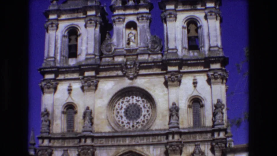1972 Portugal 8mm frame from an upward tilt across the church facade, with the rose window below upper stonework, statues, and parts of the bell towers.