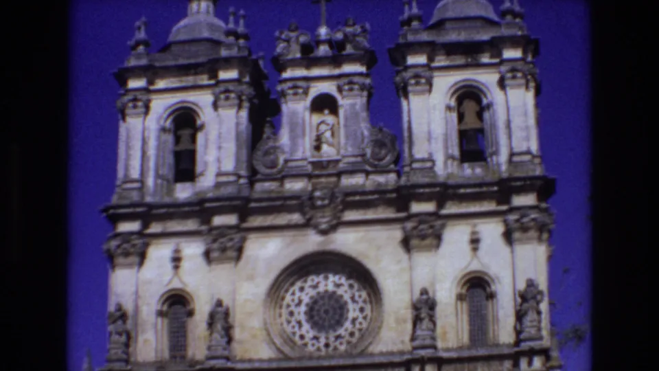 1972 Portugal 8mm frame showing the upper portion of the church with twin bell towers, carved stone ornament, a central niche, and the rose window lower in frame.
