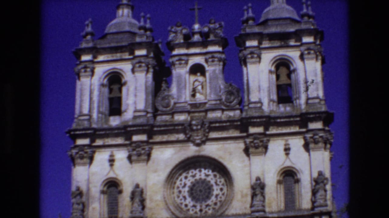 1972 Portugal 8mm frame showing the upper portion of an ornate church facade with bell openings, religious statues, a circular rose window, and saturated blue-purple sky.