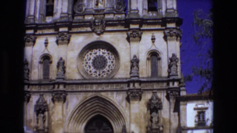 1972 Portugal 8mm frame showing the lower portion of the church facade, including the large rose window, pointed entrance arch, statues, bell openings, and saturated sky at the side.