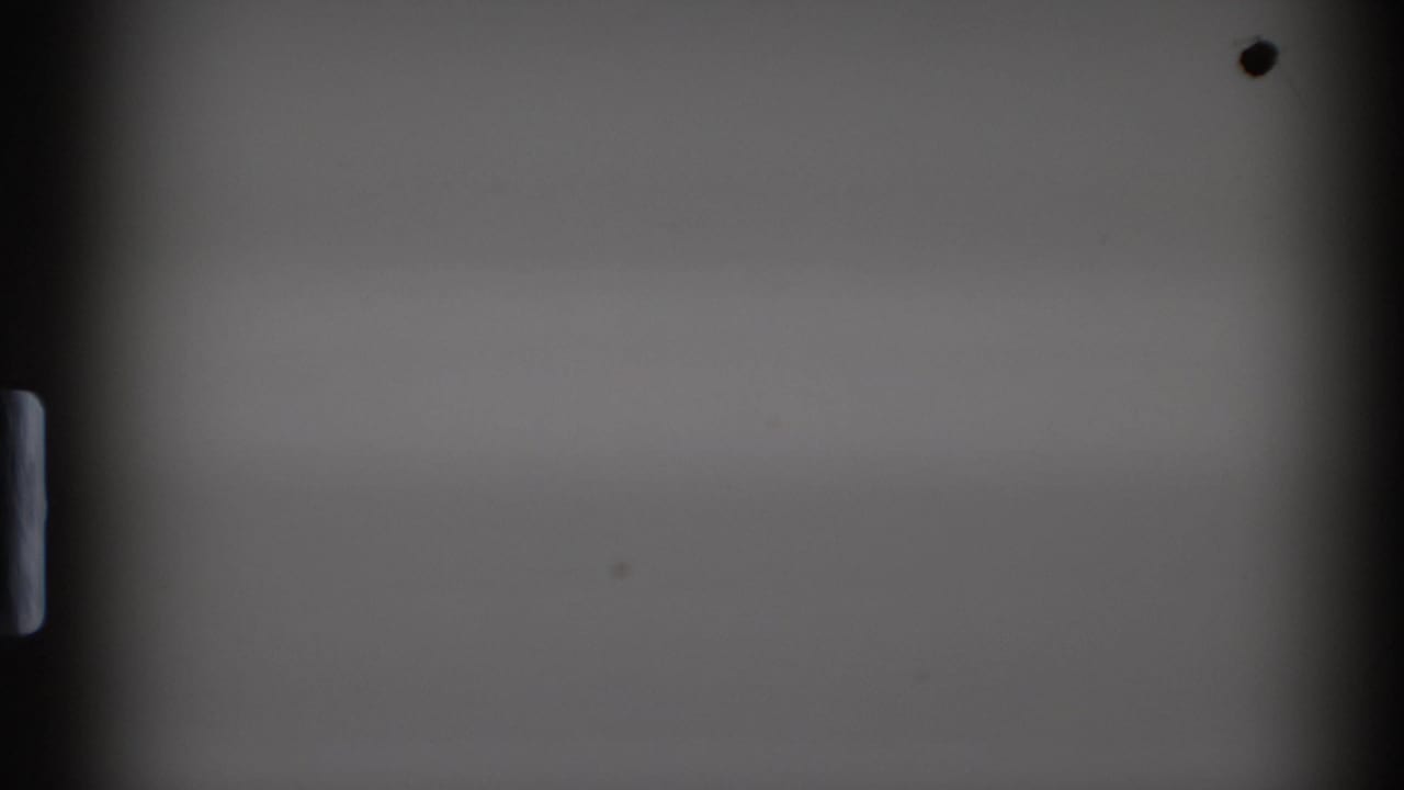 Mostly blank 8mm film frame from the 1972 clip, showing dark gate edges, sprocket detail, and small dust marks before the souvenir scene appears.