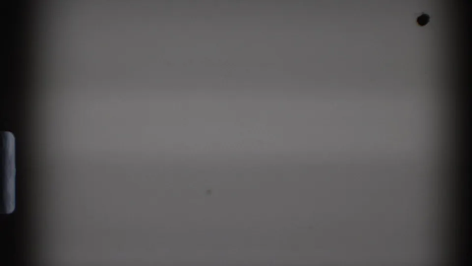 Mostly blank 8mm film frame from the 1972 clip, showing dark gate edges, sprocket detail, and small dust marks before the souvenir scene appears.