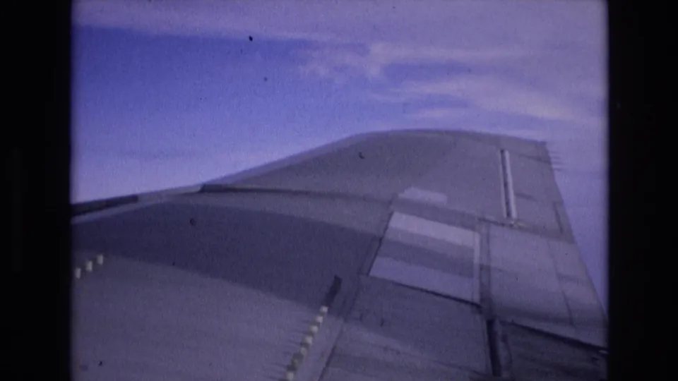 A 1972 Spain-associated 8mm frame shows the aircraft wing more clearly across the lower right, with blue sky and light cloud cover beyond the passenger window.