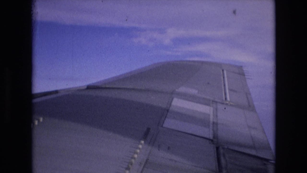 Airplane wing seen through a passenger window against a blue sky.