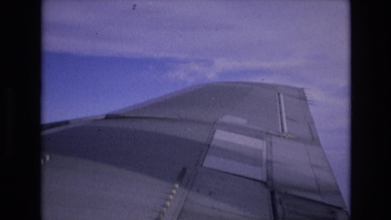 1972 Spain 8mm passenger-window view of the aircraft wing, with the wingtip and panel lines visible under a hazy blue sky.